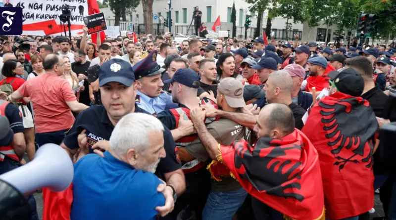 Crowded street protest with police in uniform separating demonstrators as red banners and flags wave overhead.