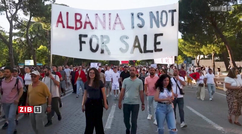 Protesters march on a city street holding a large banner that reads 'ALBANIA IS NOT FOR SALE'.