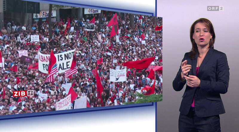 News broadcast showing a large protest crowd with red flags and signs, including 'Albania is not for sale', next to a female presenter on the right side.