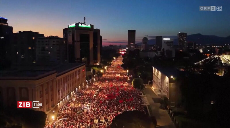 Aerial view of a crowded city street at dusk with thousands of protesters marching along a well-lit avenue between buildings.",