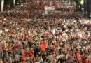 Huge protest crowd filling a wide street with red flags and signs; a banner reads 'Albania is not for sale'.