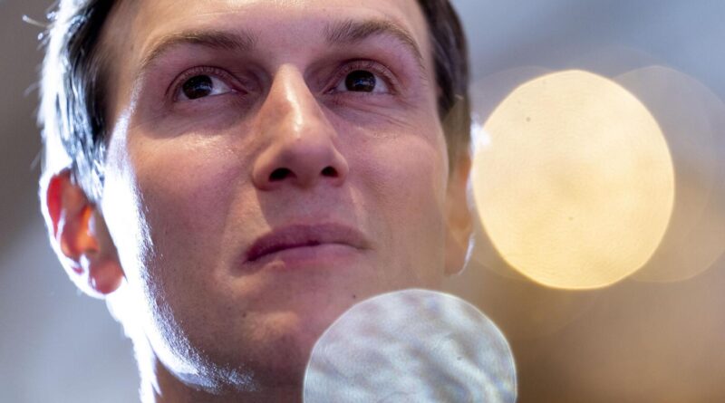 Close-up of a man looking upward, with soft stage lights in the background and a blurred microphone in front.