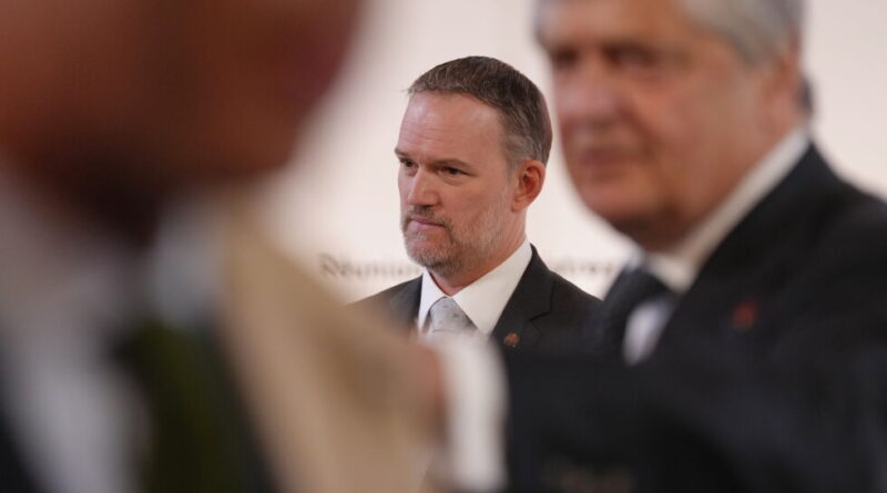 Focused man in a suit at a formal event, with two blurred figures in the foreground.