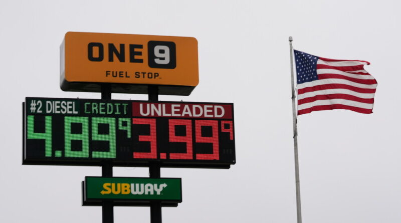 Gas station sign with orange ONE9 Fuel Stop, green diesel price and red unleaded price, plus a waving American flag nearby.