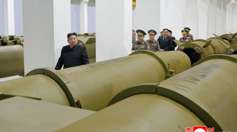 Kim Jong-un walking between large missile tubes inside a military facility, flanked by uniformed officers.