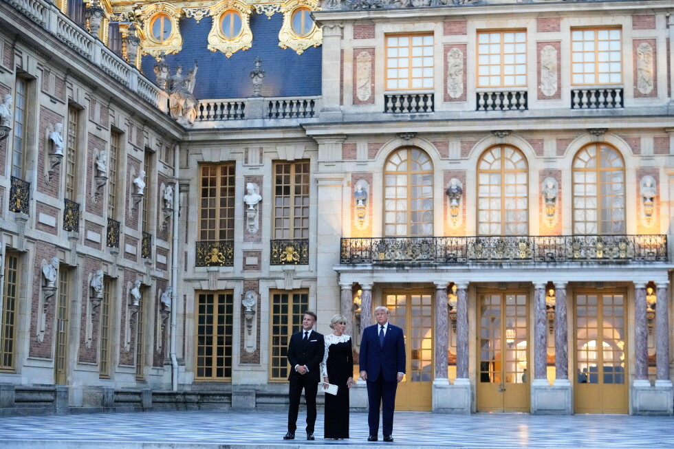 Three formally dressed adults stand on a checkered courtyard in front of an ornate historic palace façade with gold accents.