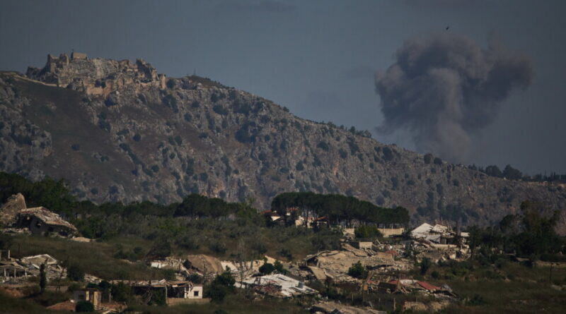 Rugged hillside with an ancient fortress on the left, a dark smoke plume rising on the right, and a small village in the foreground.