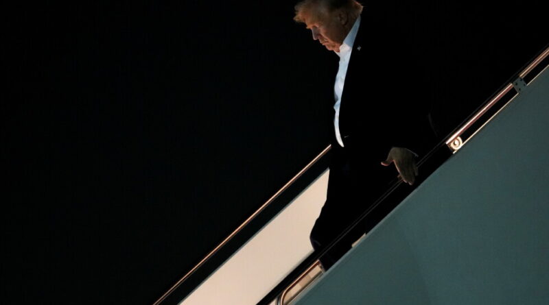 Man in a dark suit and white shirt descending an aircraft stairway at night.