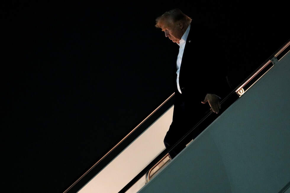 Man in a dark suit and white shirt descending an aircraft stairway at night.