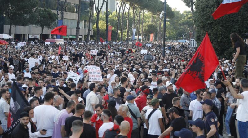 Large crowd of protesters filling a street, holding signs with Albanian flags visible in the foreground/center.