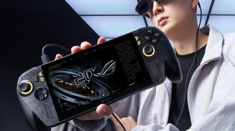 Handheld gaming console held at an angle, screen showing a futuristic design and '20th anniversary' motif, with a person wearing sunglasses in the background.