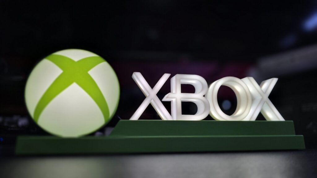 Xbox branding display: illuminated white XBOX letters beside a large lime-green sphere on a dark background, mounted on a green pedestal.